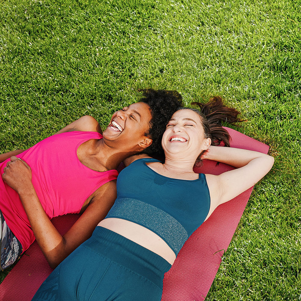 2 women laugh together on a yoga mat